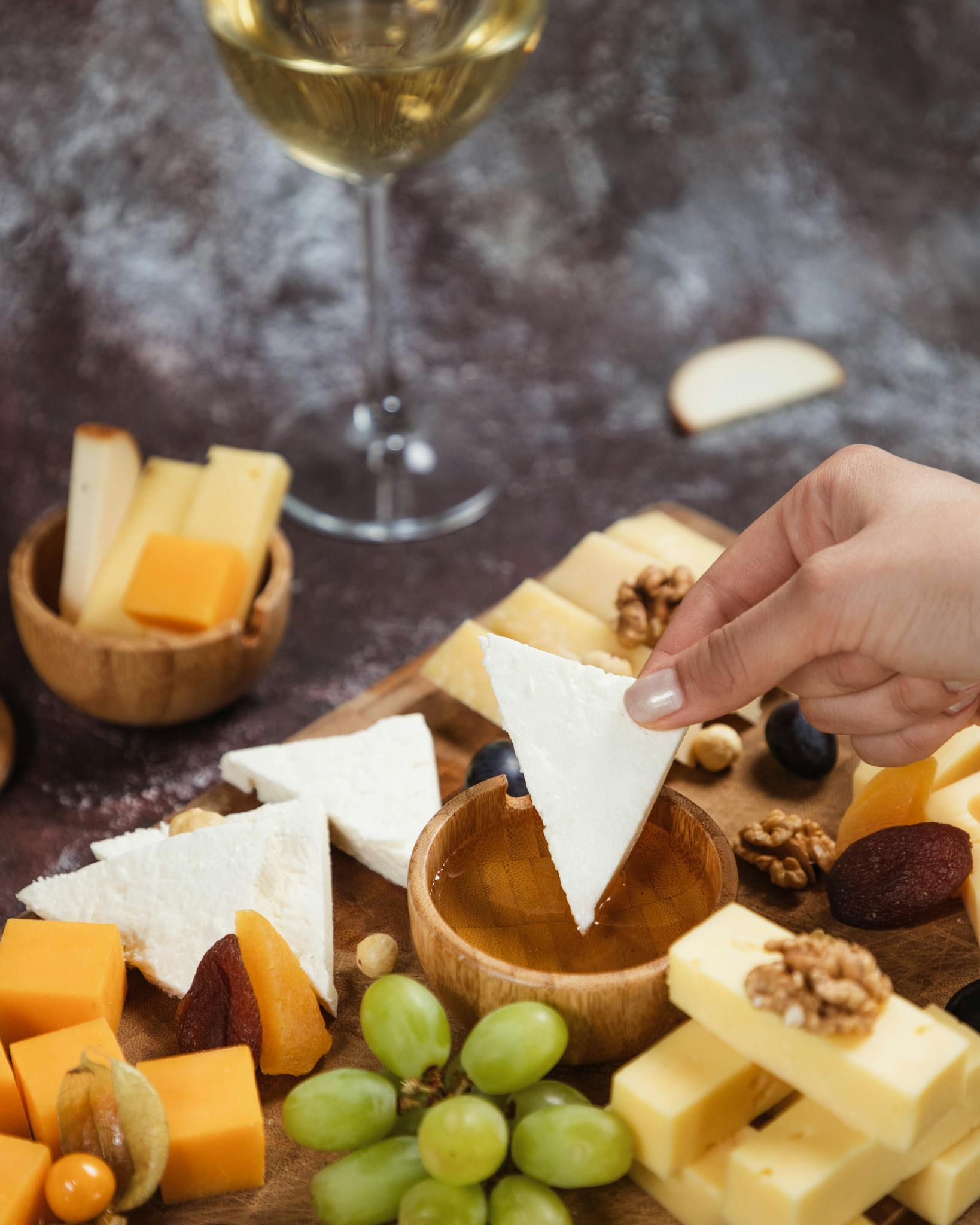 Dipping cheese into honey. Platter, snacks and white wine. Overhead